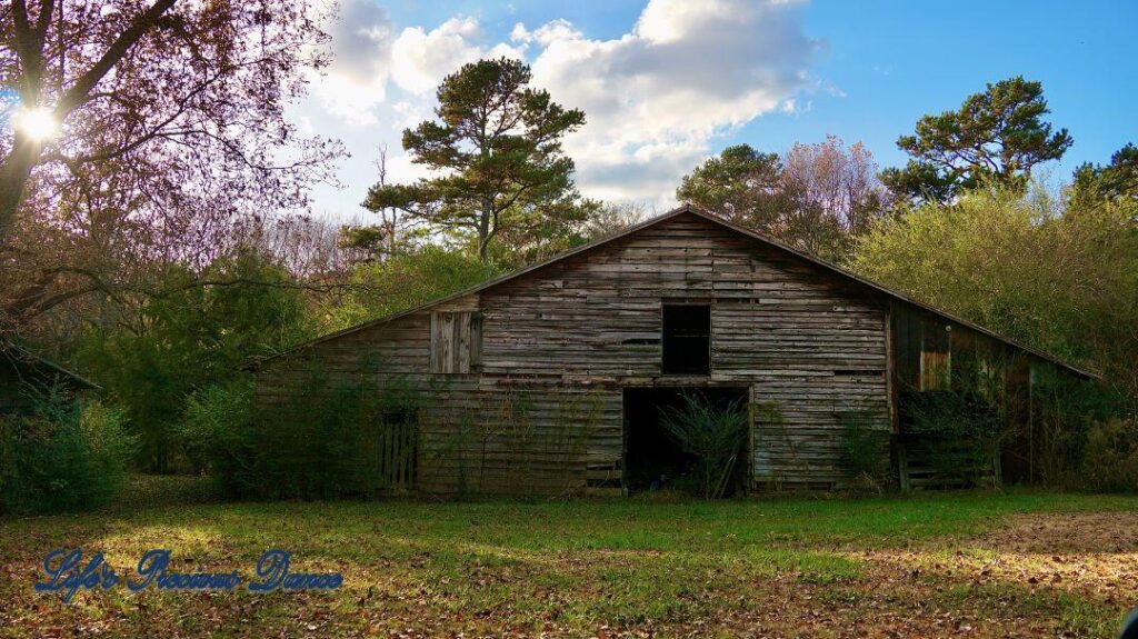 Old barn with clouds and trees in the background.