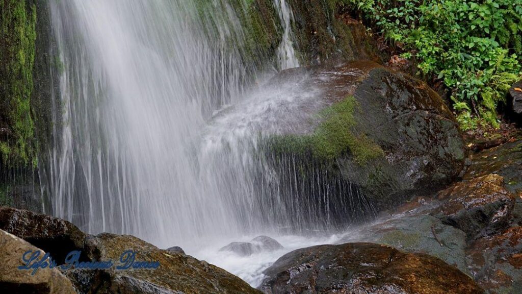 Close up of a waterfall, flowing down the mountainside, over moss covered rocks.