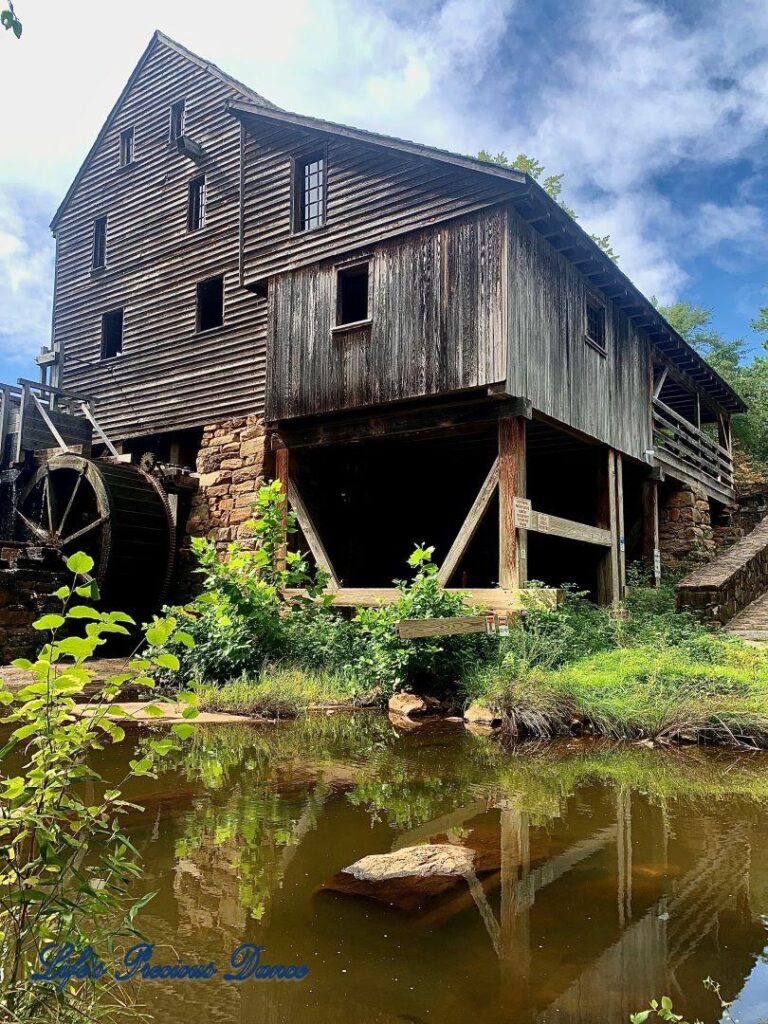 Historic Yates Mill, with blue-sky in background, beside the pond.