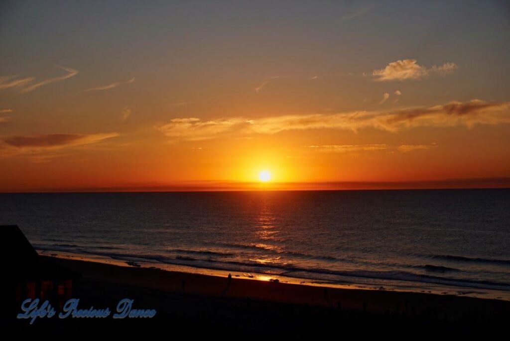 Sunrise over a calm ocean at Surfside Beach with a few clouds in sky.