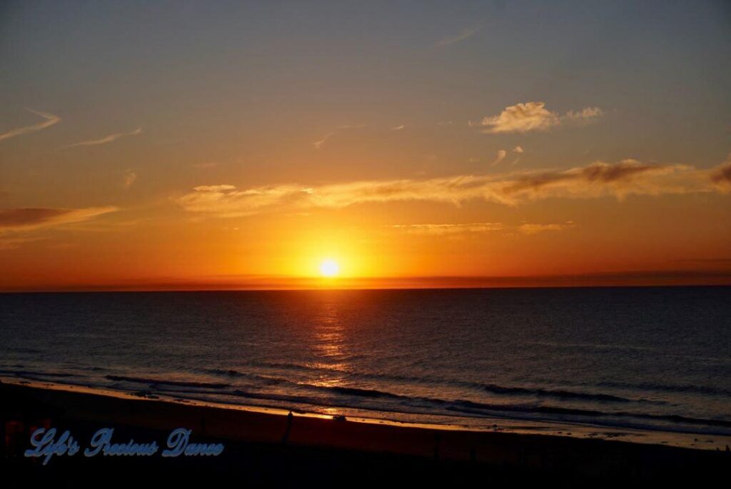 Sunrise over a calm ocean at Surfside Beach with a few clouds in sky.