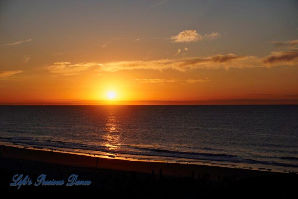 Sunrise over a calm ocean at Surfside Beach with a few clouds in sky.