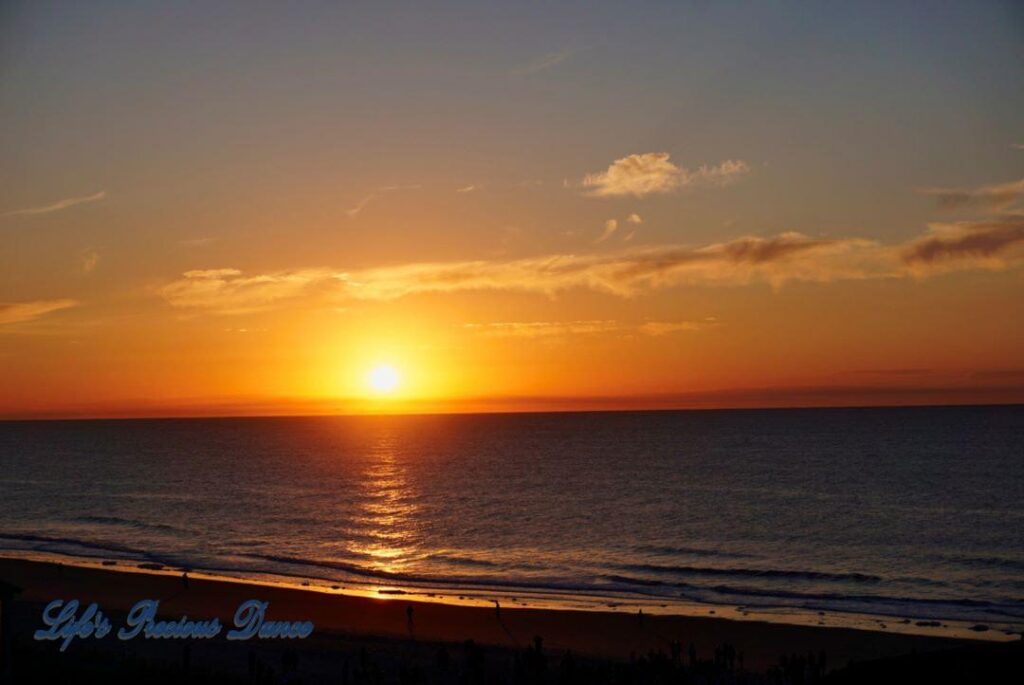 Sunrise over a calm ocean at Surfside Beach with a few clouds in sky.