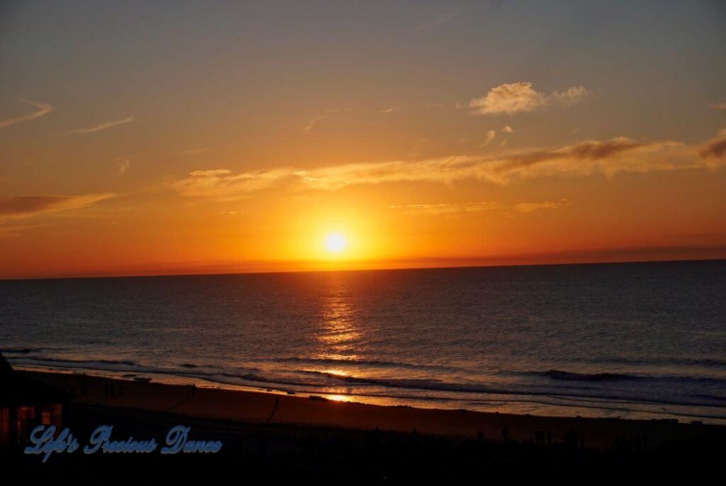 Sunrise over a calm ocean at Surfside Beach with a few clouds in sky.