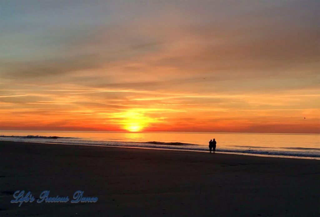 Colorful sunrise over the ocean, as waves roll in at Myrtle Beach. Couple in foreground watching..