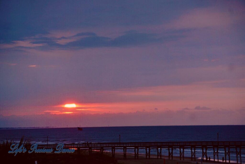 Sunrise at Ocean Isle Beach with pier and American flag in foreground