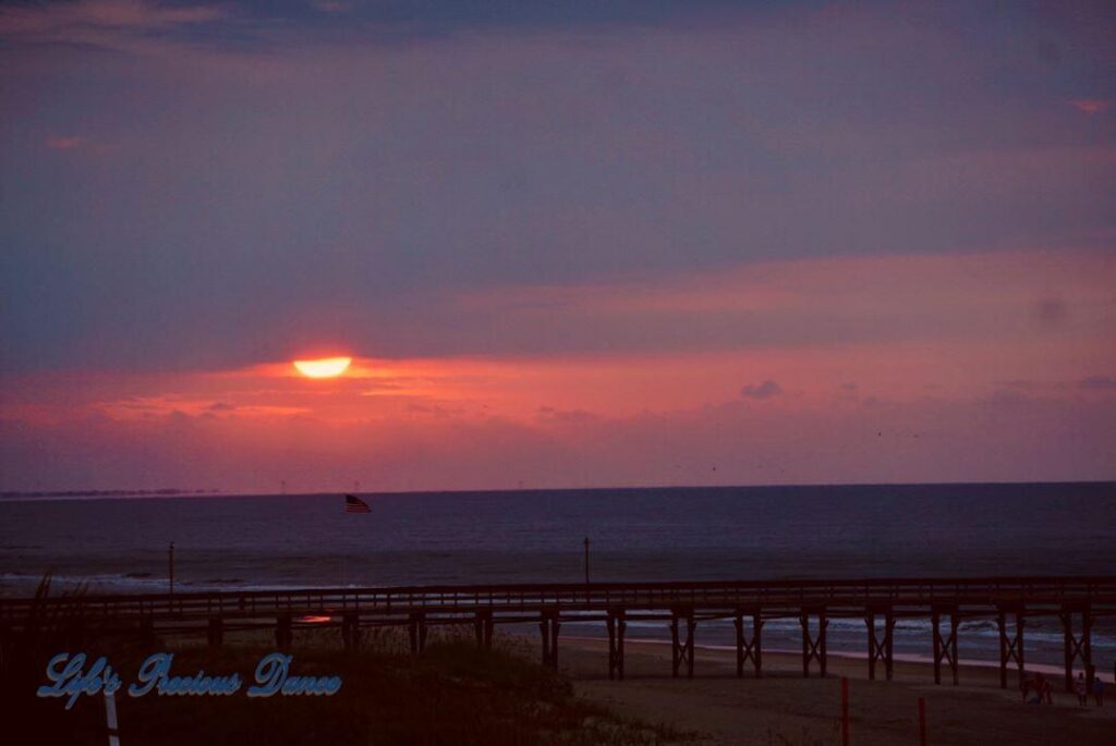 Sunrise at Ocean Isle Beach with pier and American flag in foreground