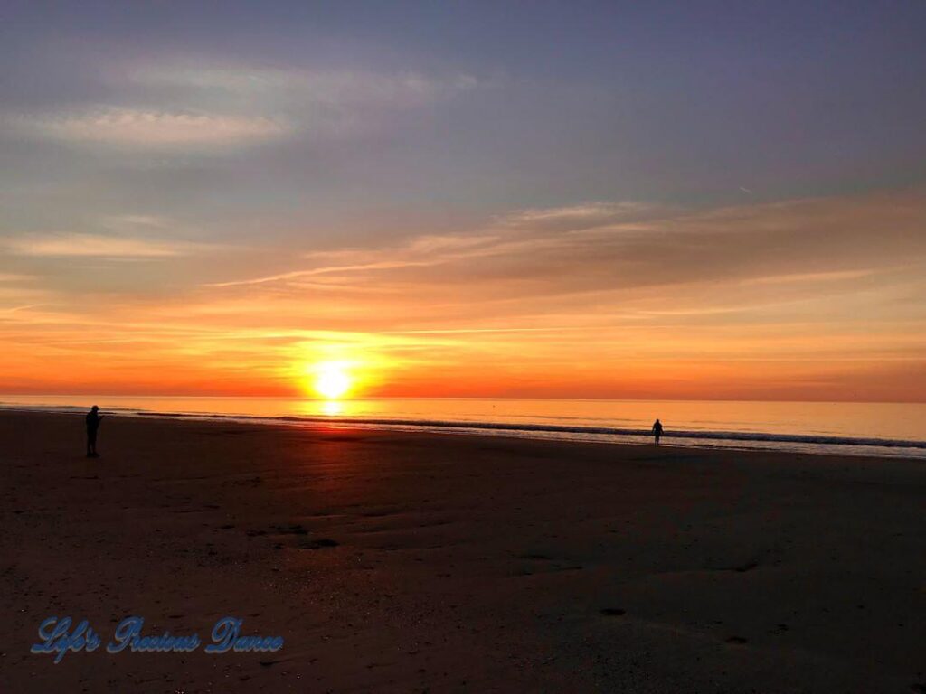 Colorful sunrise over ocean at Myrtle Beach as people stroll along the shore.