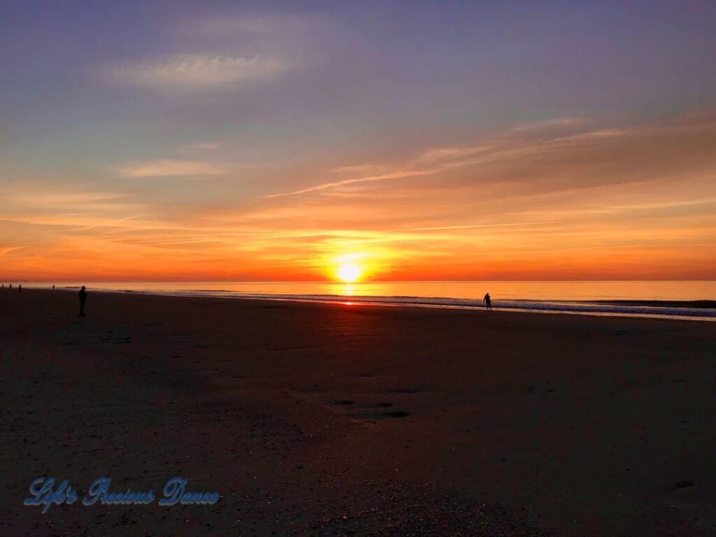 Colorful sunrise over the ocean, while people walk along the shore at Myrtle Beach