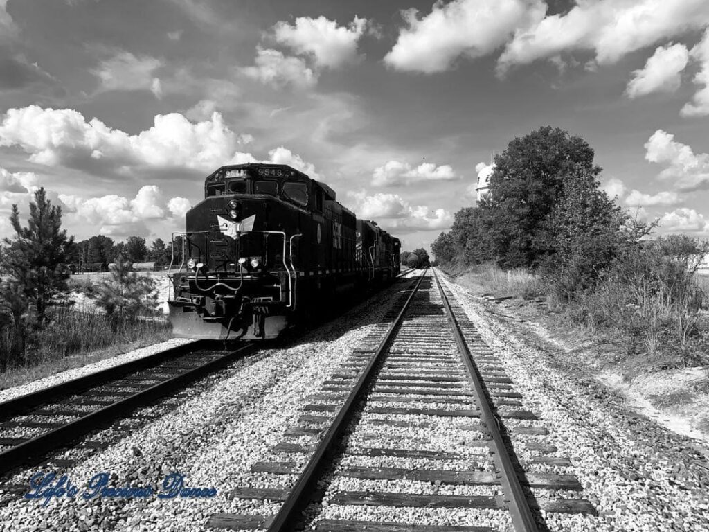 Black and white photo of a train on the tracks with clouds in the sky. Contact