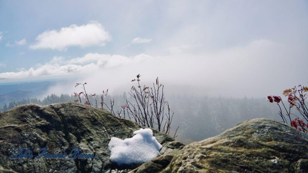 Rock outcropping with snow. partial foggy valley in background.