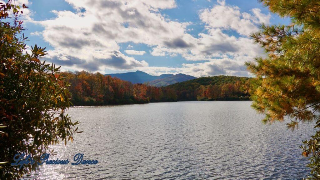 Landscape of Price Lake surrounded by colorful trees and fluffy clouds overhead. A mountain range in the background.