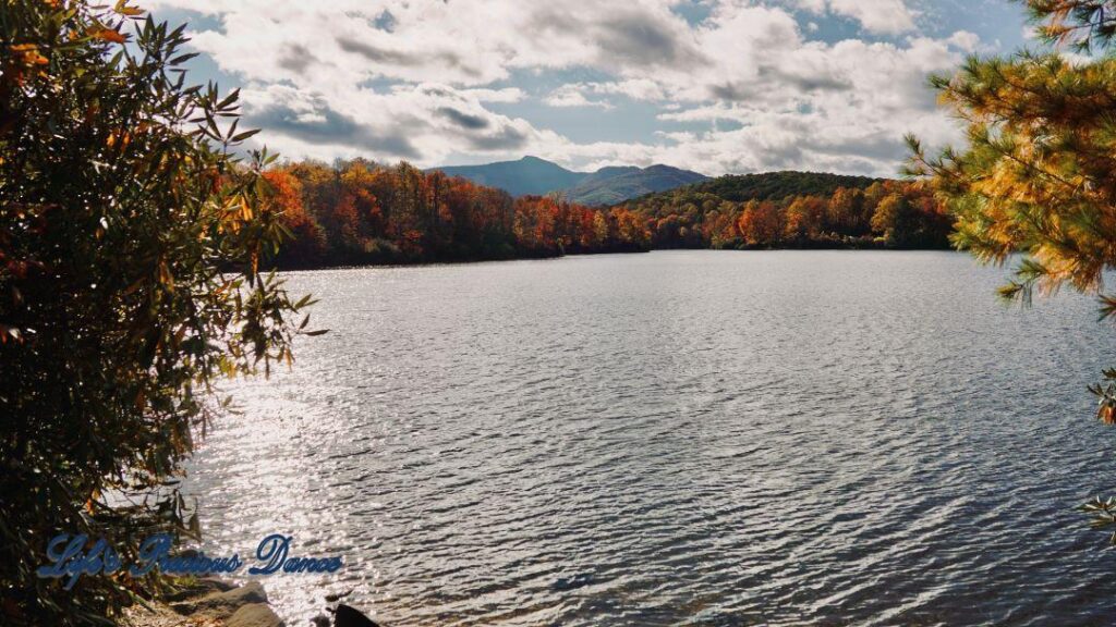 Landscape of Price Lake surrounded by colorful trees and fluffy clouds overhead. A mountain range in the background.