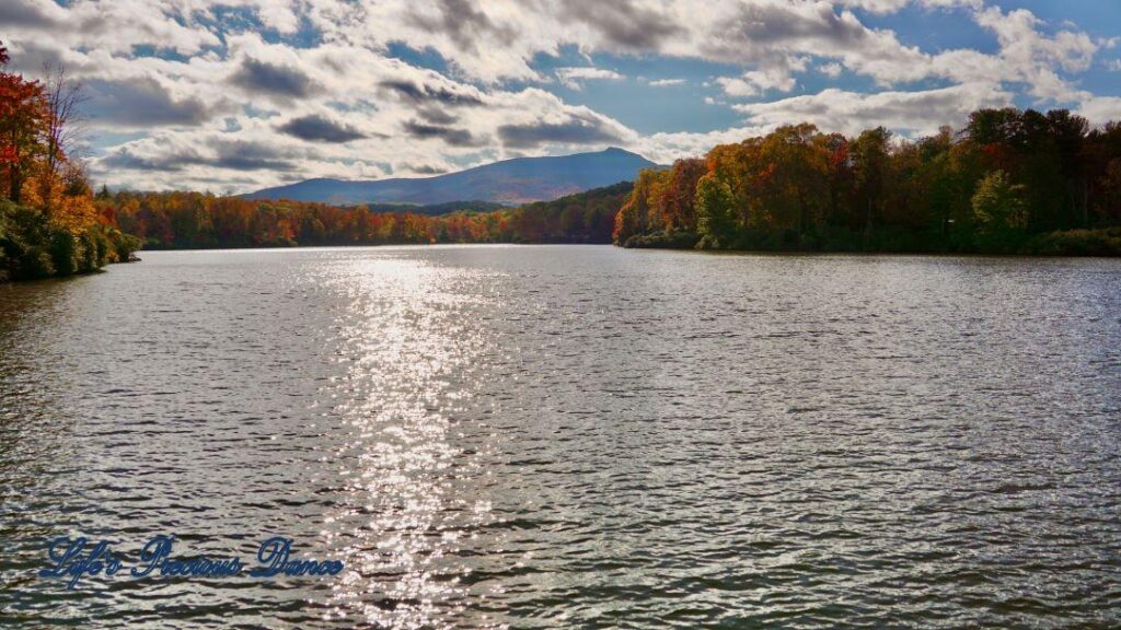 Landscape of Price Lake surrounded by colorful trees and fluffy clouds overhead. A mountain range in the background.