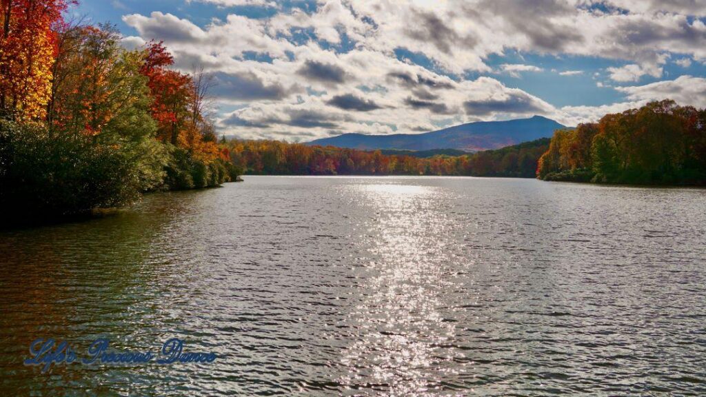 Landscape of Price Lake surrounded by colorful trees and fluffy clouds overhead. A mountain range in the background.