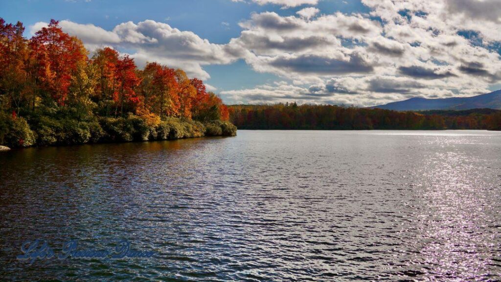 Landscape of Price Lake surrounded by colorful trees and fluffy clouds overhead. A mountain range in the background.