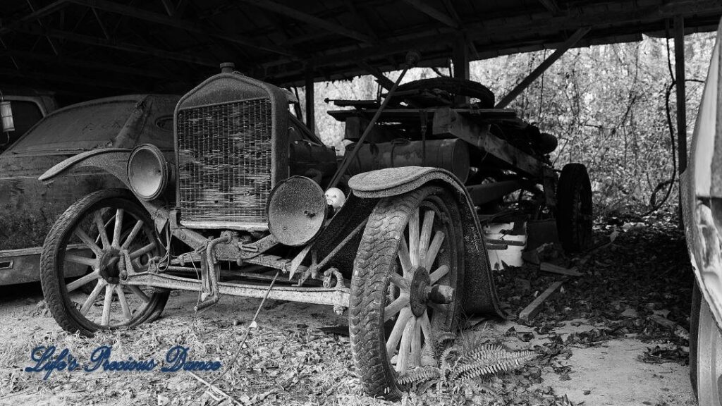 Black and white of a vintage junk car under a overhang.