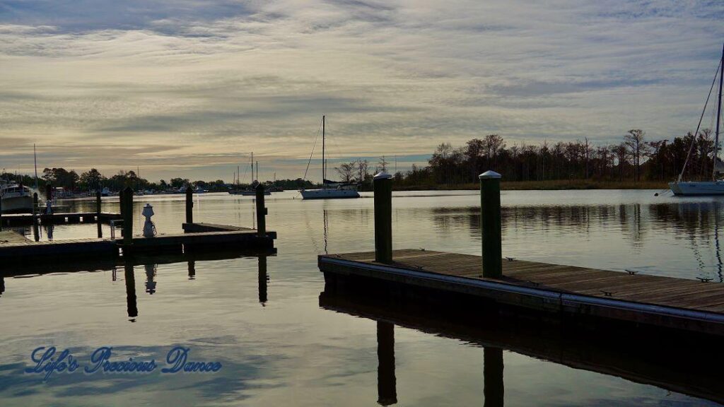 Sailboats resting in the harbor. Docks and clouds reflecting in the water