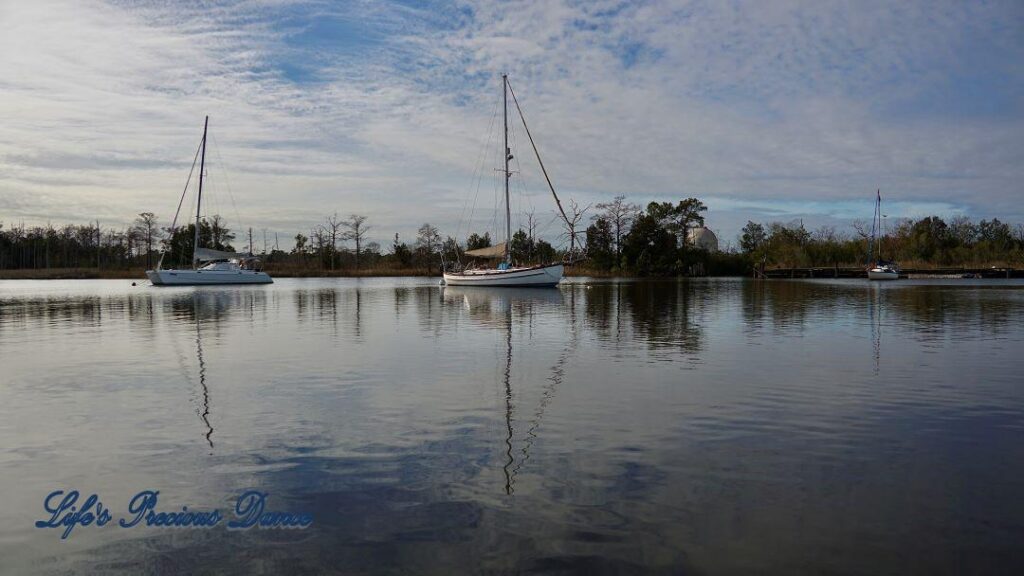 Sailboats resting in the harbor, reflecting along with clouds in the water.