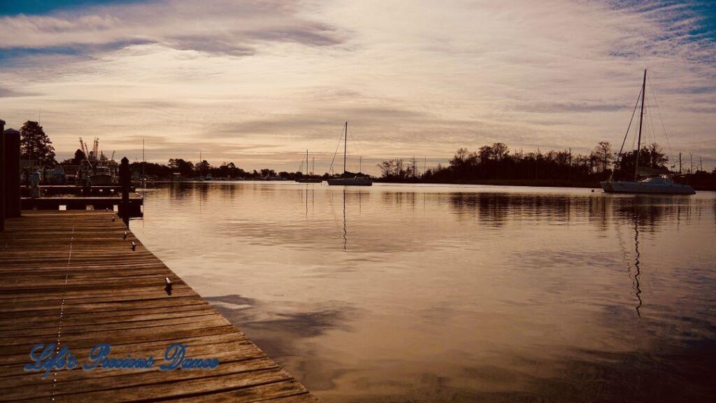 Sailboats resting and reflecting in the harbor. A dock in the foreground