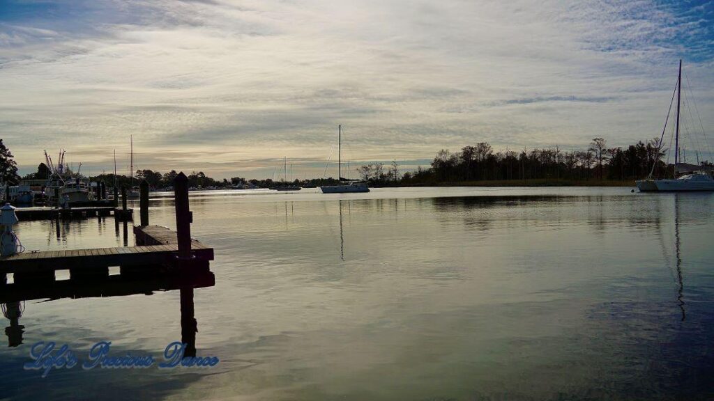 Sailboats, docks and clouds reflecting in the water of a harbor.