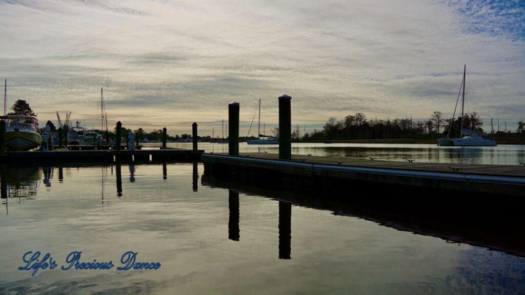 Sailboats, docks and clouds reflecting in the water of a harbor.