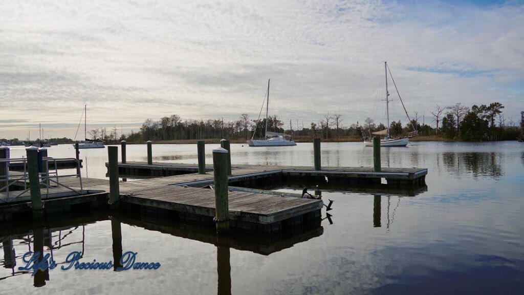 Sailboats, docks and clouds reflecting in the water of a harbor.