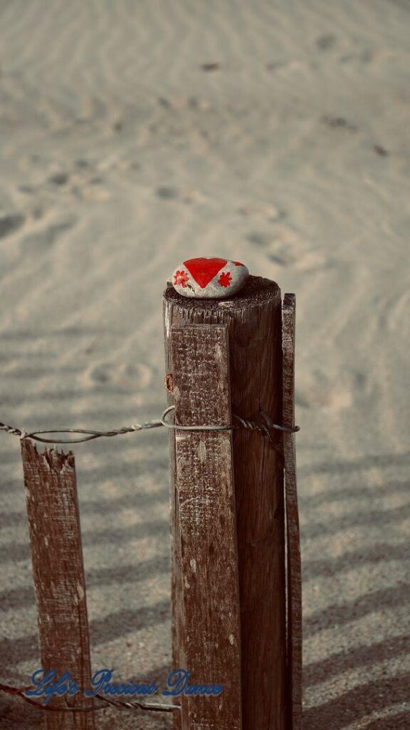 Rock with painted heart on top of fence post on the beach