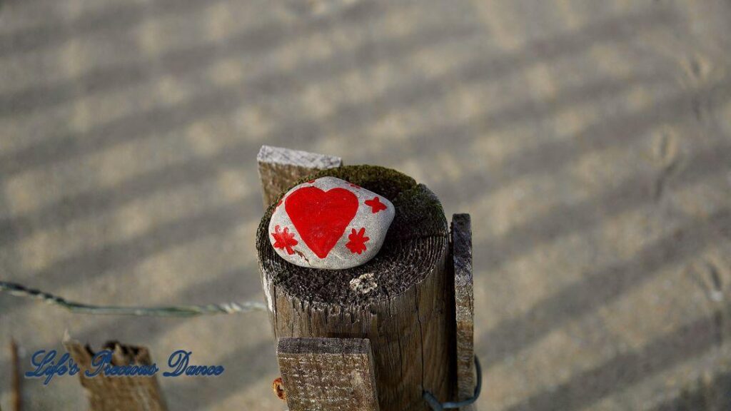 Rock with painted heart on top of fence post on the beach