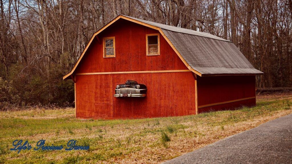 Rust colored barn with front end of classic DeSoto automobile hood protruding from structure.