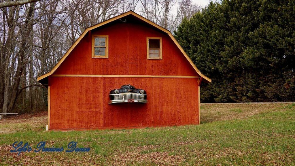 Rust colored barn with front end of classic DeSoto automobile hood protruding from structure.