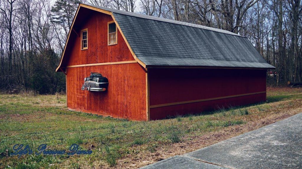 Rust colored barn with front end of classic DeSoto automobile hood protruding from structure.