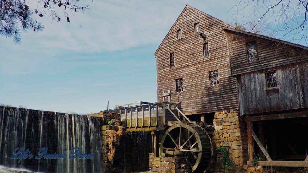 Historic Yates MIll towering above rockwall with pond water cascading into creek below.