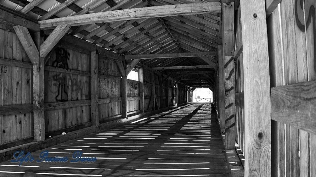 Black and white of Inside of Ole Gilliam covered bridge, sun glistening through wood slats.