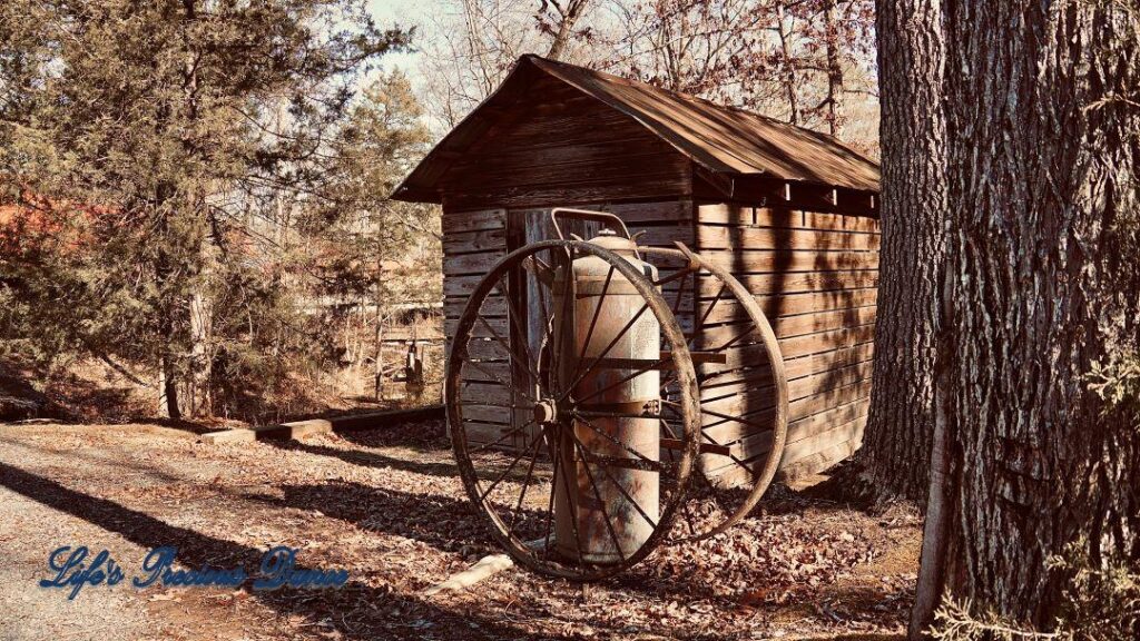 Two wagon wheels around an old tank, in front of a rustic cabin.