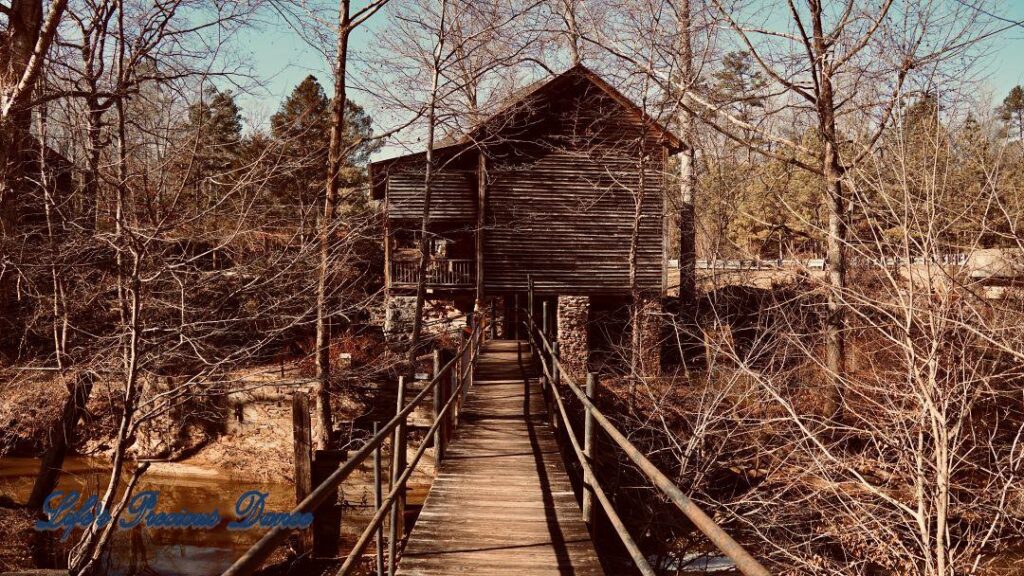 Small wooden walking bridge over creek, leading to mill.