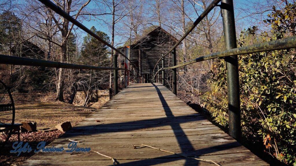 Small wooden walking bridge over creek, leading to mill. View from base of structure.