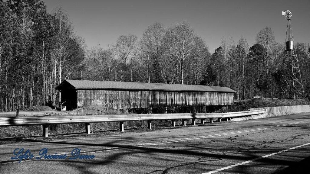 Black and white landscape view of Ole Gilliam Covered Bridge with the windmill towering above.