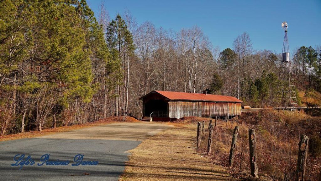 Landscape view of Ole Gilliam Covered Bridge with the windmill towering above and an old winding fence to the right.