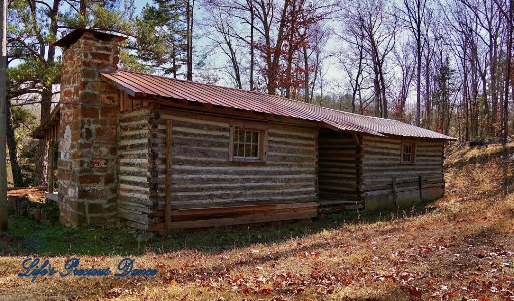 Rear view of an old wooden cabin with a stone fireplace.