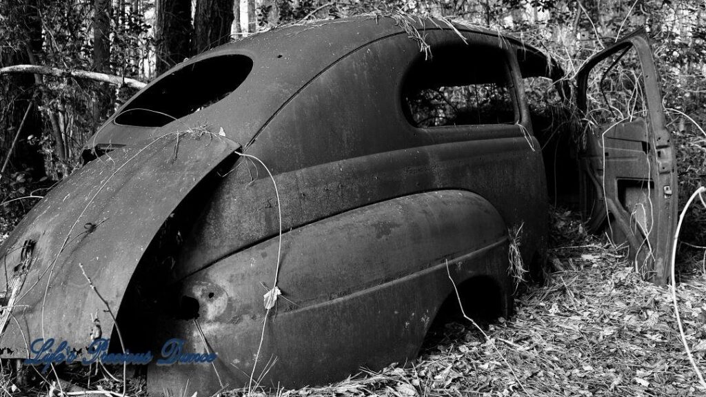 Black and white of vintage junk car in the woods.