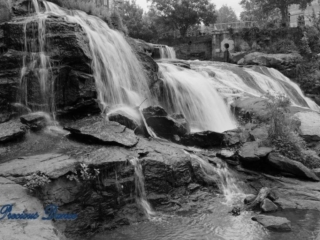Black and white of Reedy Falls cascading over a tiered rock face into the river below.