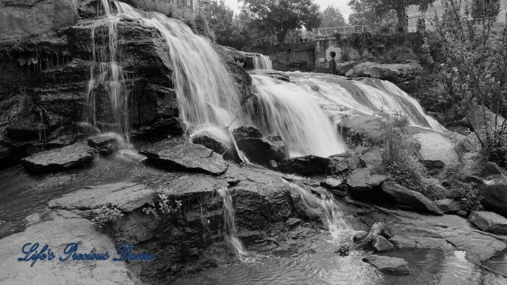 Black and white of Reedy Falls cascading over a tiered rock face into the river below.