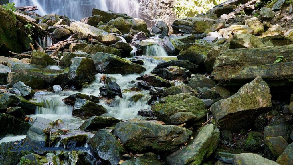 Water flowing through and spilling over rocks into a mountain stream. Waterfall in the background.