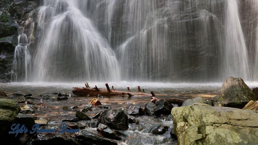 Crabtree Falls cascading down rockface into a pool of water. Rocks and a downed tree in foreground.