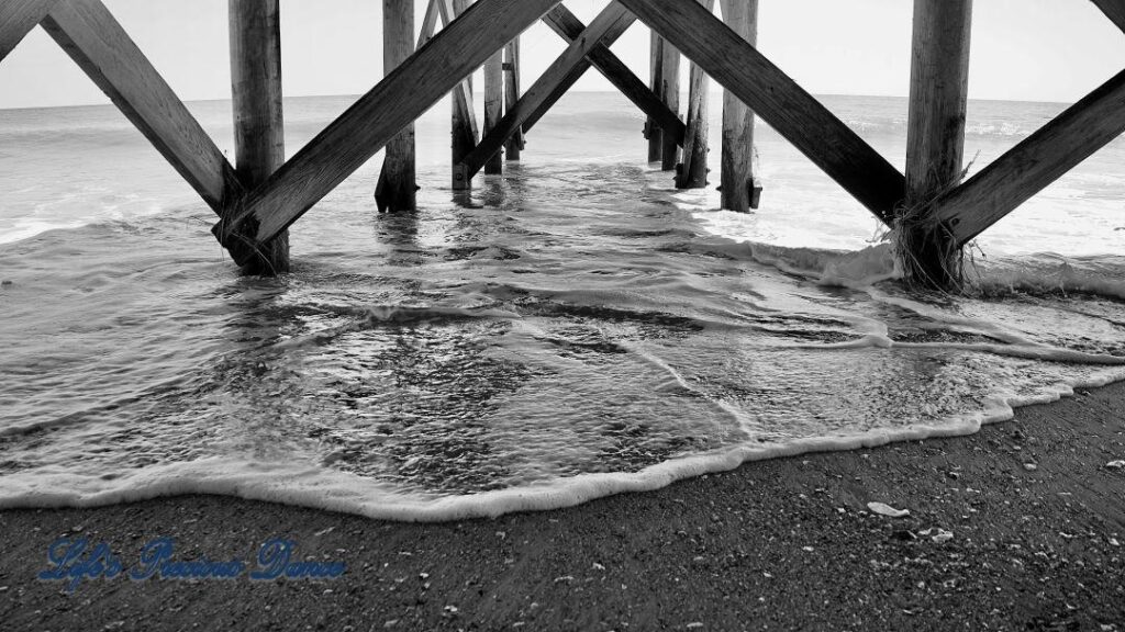 Black and white of view from under a pier as waves come crashing in at Edisto Beach.