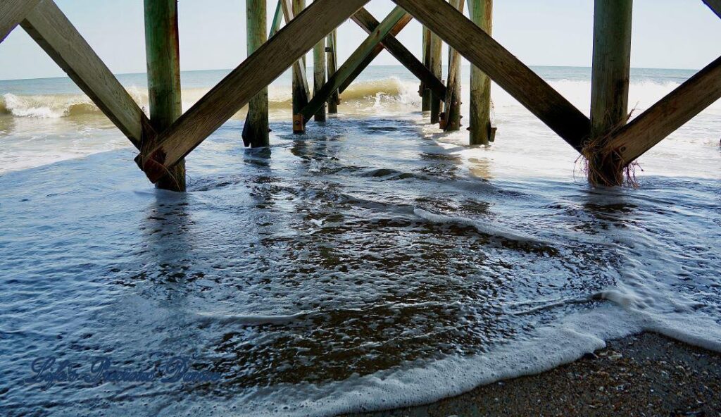 View from under a pier as waves come crashing in.