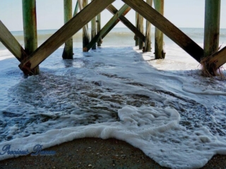 View from under a pier as foamy waves come rolling in at Edisto Beach.