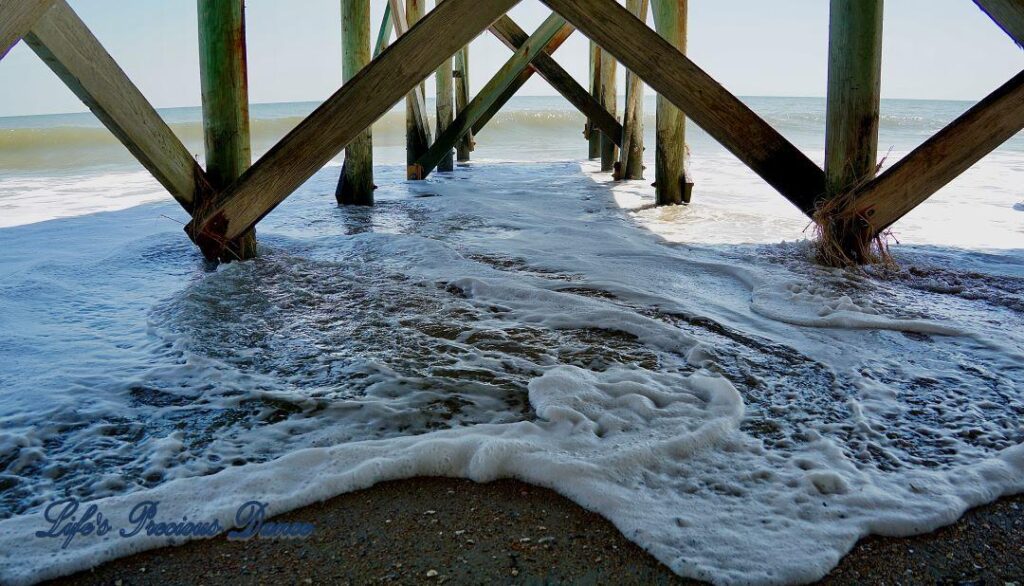 View from under a pier as foamy waves come rolling in at Edisto Beach.