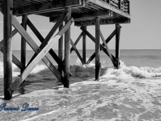 Black and white side view of waves crashing into a pier.
